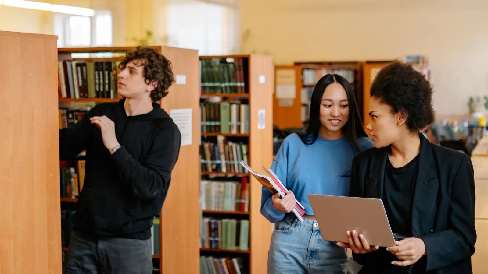 três jovens estudantes numa biblioteca da faculdade